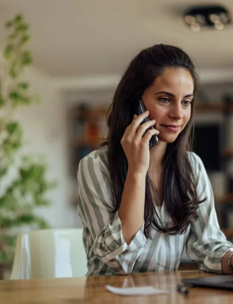 Une jeune femme travail en ligne de chez elle devant son ordinateur portable tout en téléphonant