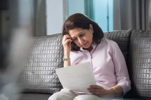 Femme seule chez elle entrain de lire un document sur son canapé