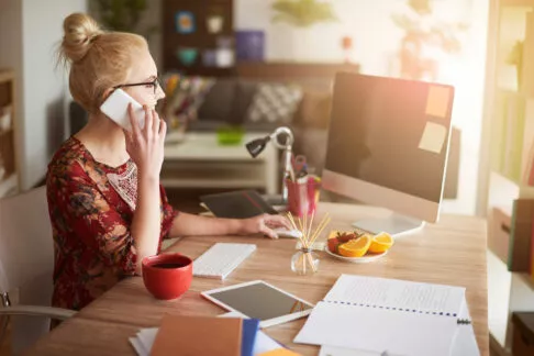 Jeune femme entourée de son ordinateur et de sa tablette tactile, travaille tout en étant au téléphone