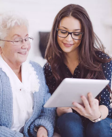 Une jeune fille montrant à sa grand mère comment se servir d'une tablette tactile