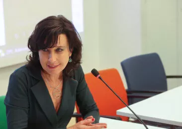 Frédérique Cintrat s'exprimant à la table du Lab OCIRP Autonomie, assise au micro sur une chaise verte, une chaise orange et une chaise noire vides à côté d'elle